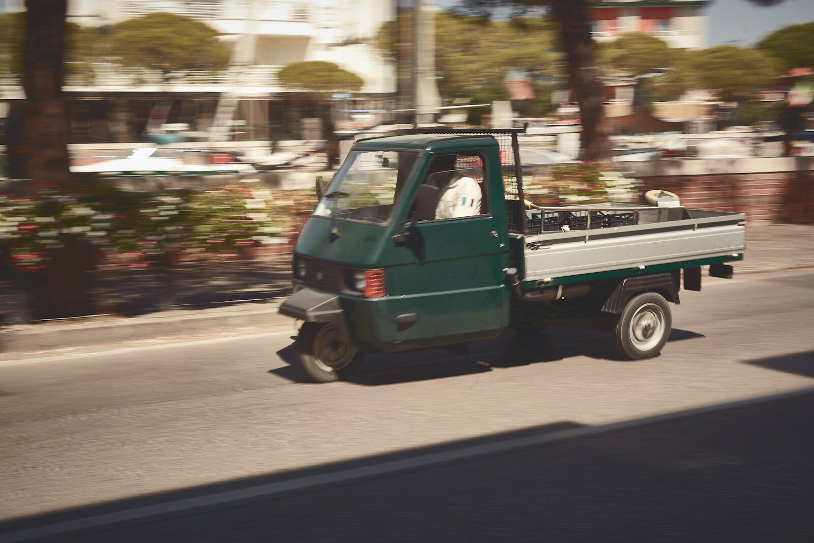 a small green truck driving down a street
